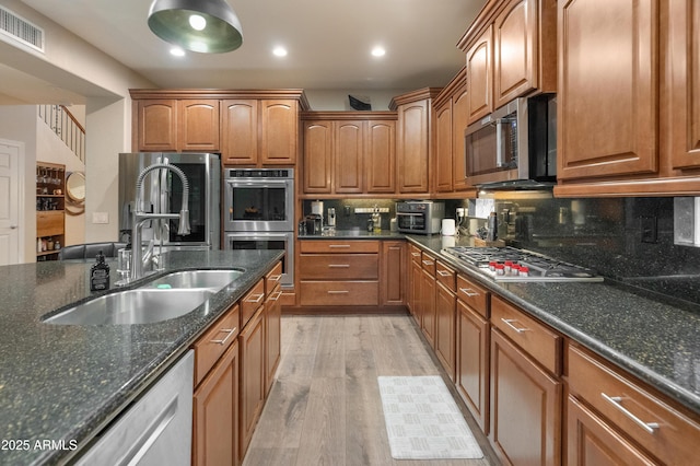 8447 W Tether Trl, Peoria, AZ 85383 - kitchen with appliances with stainless steel finishes, light wood-type flooring, decorative backsplash, brown cabinetry, and dark stone countertops