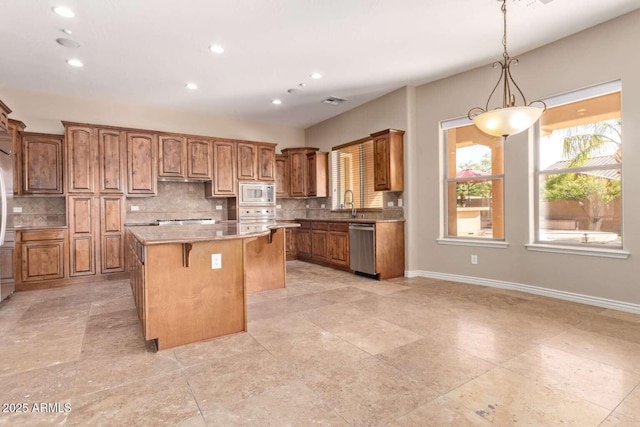 kitchen featuring appliances with stainless steel finishes, a center island, tasteful backsplash, hanging light fixtures, and a breakfast bar area