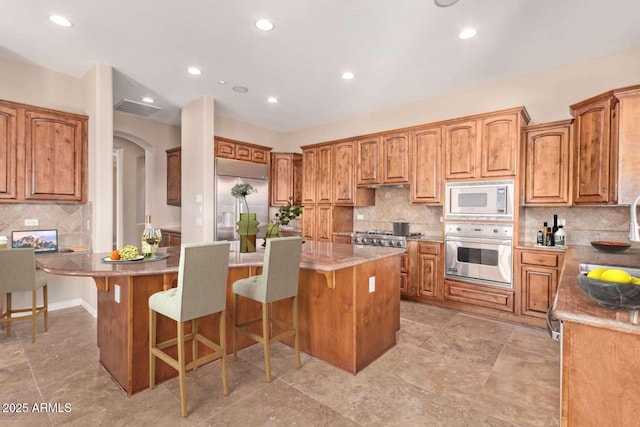 kitchen with a kitchen island, decorative backsplash, a breakfast bar, and built in appliances