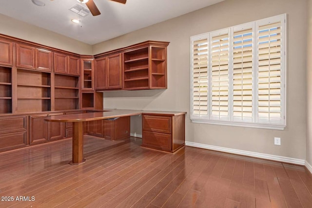 unfurnished office featuring ceiling fan, plenty of natural light, built in desk, and dark wood-type flooring