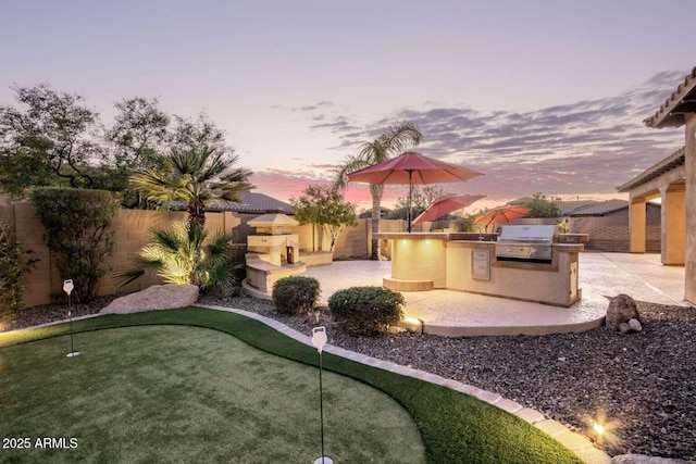 yard at dusk featuring exterior kitchen and a patio