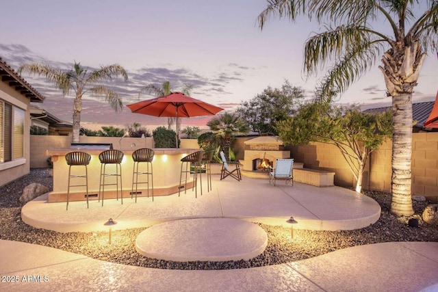 patio terrace at dusk with an outdoor bar and an outdoor stone fireplace