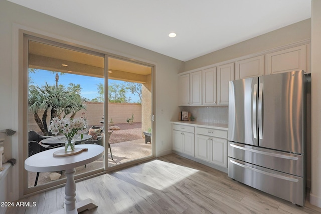 kitchen with backsplash, stainless steel refrigerator, white cabinetry, and light hardwood / wood-style flooring