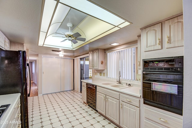 kitchen featuring a tray ceiling, ceiling fan, sink, and black appliances