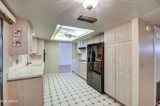 kitchen featuring white gas cooktop, black fridge, sink, a skylight, and a textured ceiling