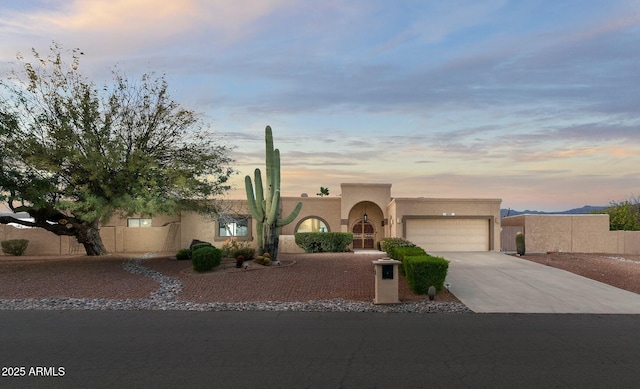 pueblo revival-style home with a garage, concrete driveway, fence, and stucco siding