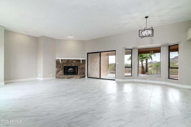 unfurnished living room with a chandelier, plenty of natural light, a stone fireplace, and baseboards