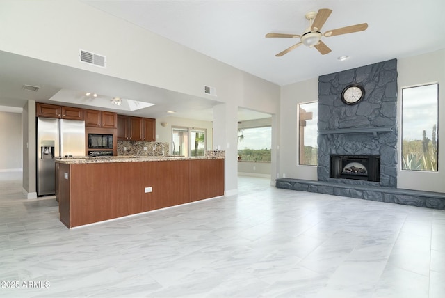 kitchen with black microwave, a stone fireplace, visible vents, open floor plan, and stainless steel fridge