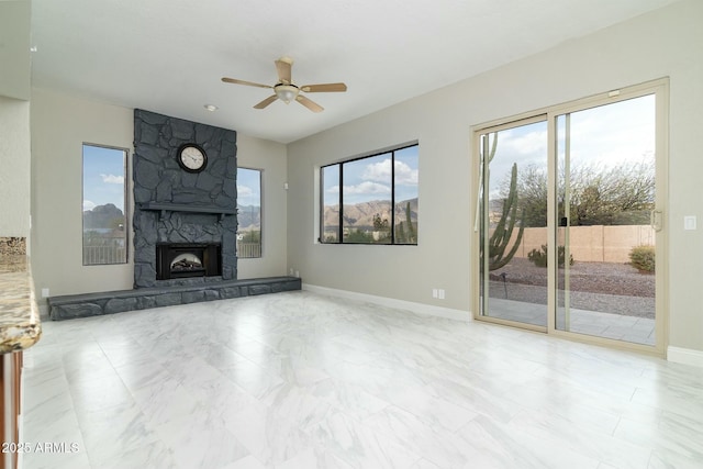 unfurnished living room with ceiling fan, a stone fireplace, and baseboards