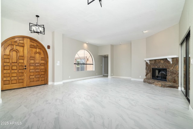 unfurnished living room featuring marble finish floor, a fireplace, baseboards, and a notable chandelier