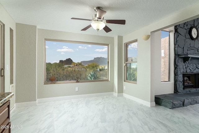 interior space with marble finish floor, ceiling fan, a stone fireplace, and baseboards