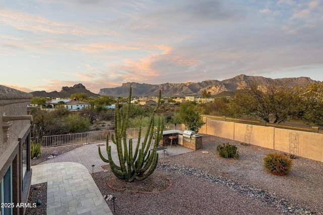 yard at dusk with a patio area, a mountain view, and a fenced backyard