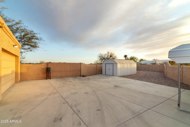 patio terrace at dusk with a storage unit, an outdoor structure, and a fenced backyard