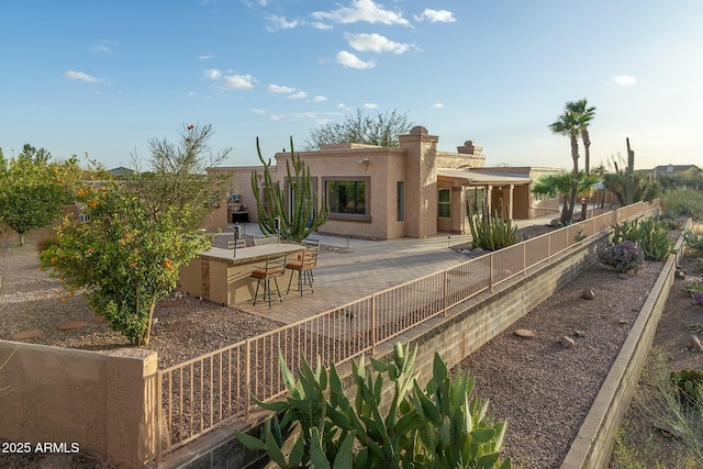 rear view of house with a chimney, outdoor dry bar, fence, a patio area, and stucco siding