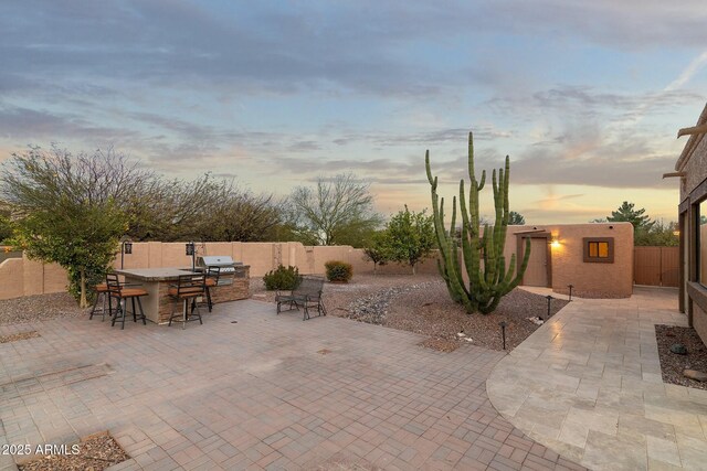 patio terrace at dusk with outdoor dry bar, grilling area, a fenced backyard, and area for grilling