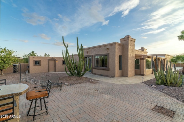 rear view of property with stucco siding, a chimney, an outbuilding, and a patio