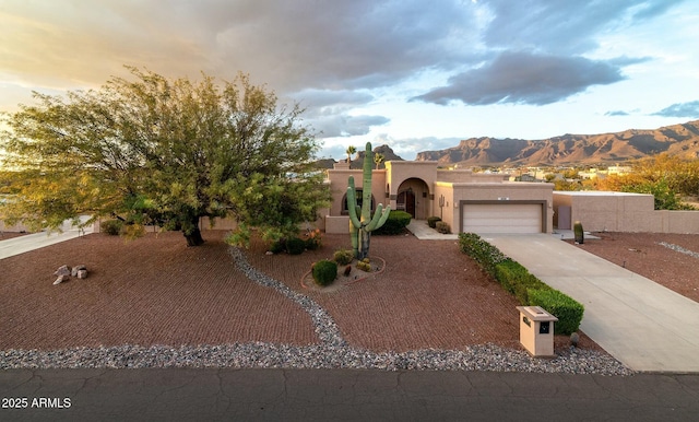 adobe home with concrete driveway, an attached garage, a mountain view, and stucco siding