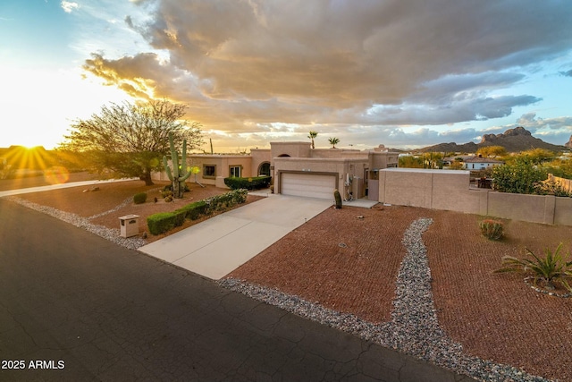 pueblo-style house featuring a garage, driveway, fence, and stucco siding