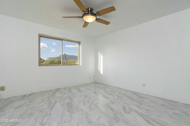 empty room featuring marble finish floor, ceiling fan, and baseboards