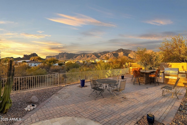 view of patio with grilling area, fence, exterior kitchen, a mountain view, and outdoor dining space