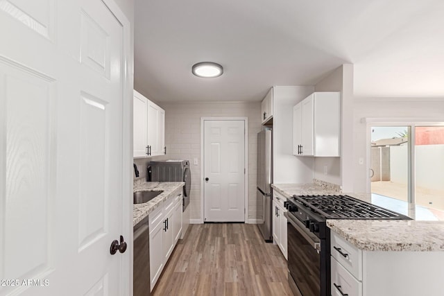 3812 W Seldon Ln, Phoenix, AZ 85051 - kitchen featuring appliances with stainless steel finishes, washer and dryer, light wood-style floors, white cabinetry, and light stone counters
