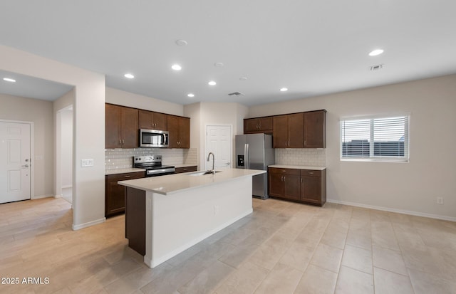 kitchen with sink, tasteful backsplash, dark brown cabinets, a center island with sink, and appliances with stainless steel finishes