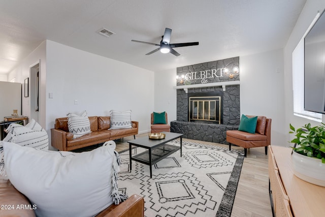 living room featuring a stone fireplace, ceiling fan, and light hardwood / wood-style floors