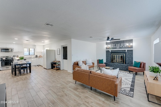 living room featuring a stone fireplace, ceiling fan, and a textured ceiling