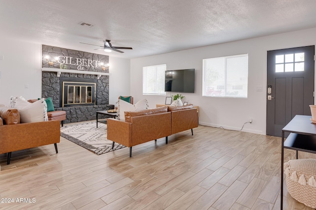 living room with ceiling fan, a fireplace, a textured ceiling, and light hardwood / wood-style flooring