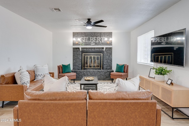 living room featuring a fireplace, ceiling fan, a textured ceiling, and light hardwood / wood-style flooring