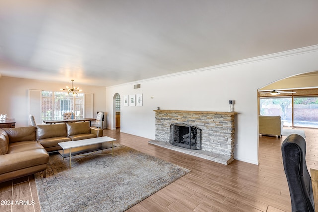 living room featuring an inviting chandelier, a stone fireplace, light hardwood / wood-style floors, and crown molding