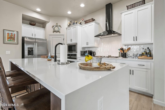 kitchen with a large island with sink, white cabinetry, stainless steel appliances, and wall chimney range hood