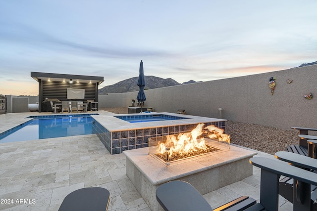 pool at dusk with an in ground hot tub, a patio, a mountain view, and an outdoor fire pit