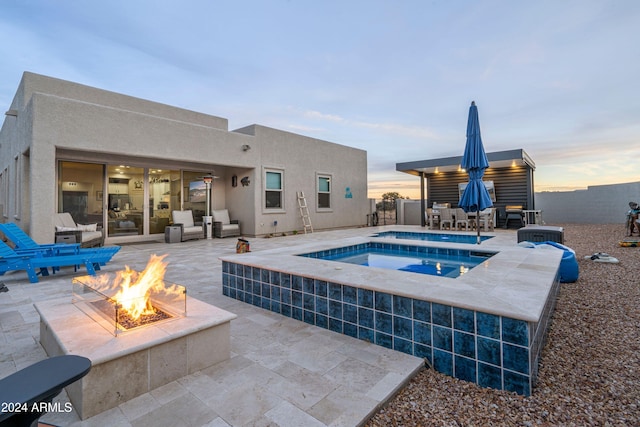 pool at dusk featuring an in ground hot tub, a patio, and an outdoor living space with a fire pit