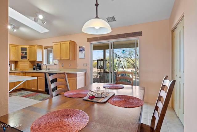 tiled dining space with vaulted ceiling with skylight and sink