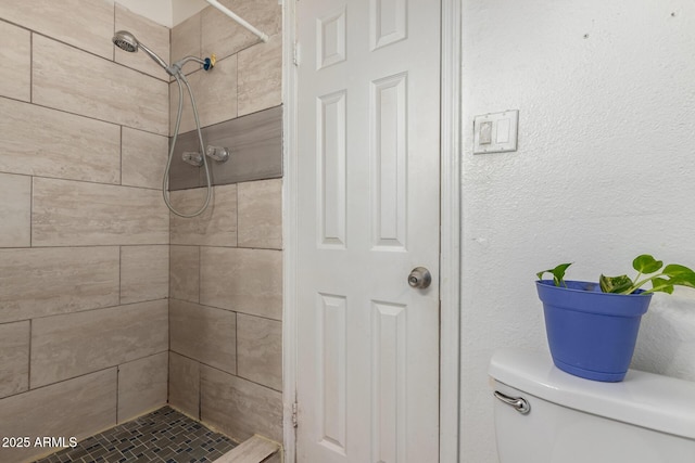 bathroom featuring toilet, tiled shower, and a textured wall