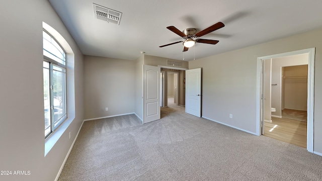 unfurnished bedroom featuring ceiling fan, a spacious closet, light colored carpet, and a closet