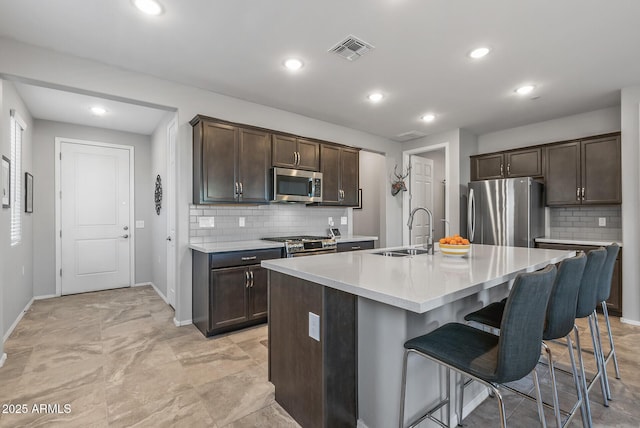 kitchen with sink, backsplash, a kitchen island with sink, a breakfast bar area, and stainless steel appliances