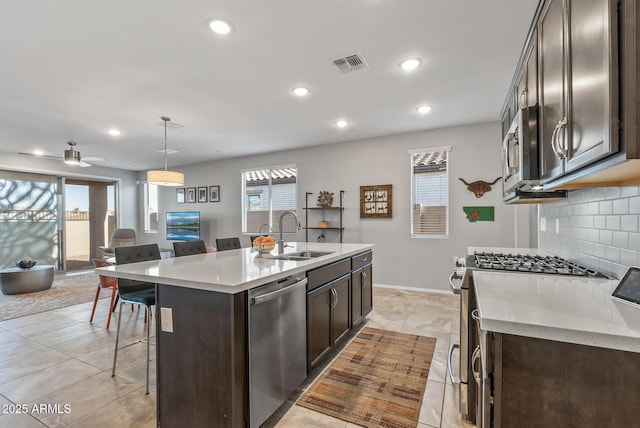 kitchen featuring appliances with stainless steel finishes, a kitchen island with sink, sink, pendant lighting, and a breakfast bar