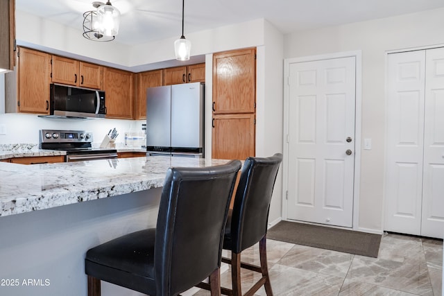 kitchen featuring brown cabinets, light stone counters, a kitchen breakfast bar, stainless steel appliances, and a peninsula