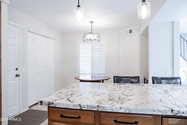 kitchen with visible vents, hanging light fixtures, light stone countertops, brown cabinets, and a chandelier