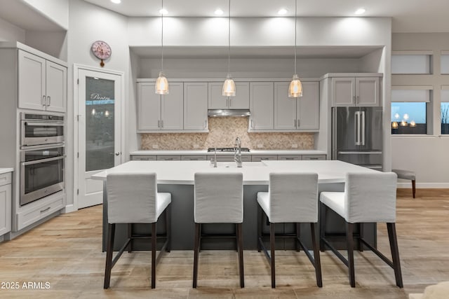 kitchen with gray cabinetry, a kitchen island with sink, decorative light fixtures, and appliances with stainless steel finishes