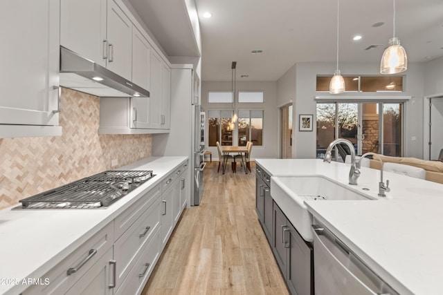 kitchen with sink, stainless steel appliances, hanging light fixtures, backsplash, and light wood-type flooring