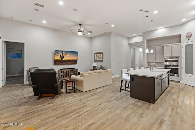 kitchen with ceiling fan, hanging light fixtures, decorative backsplash, a kitchen island with sink, and white cabinets