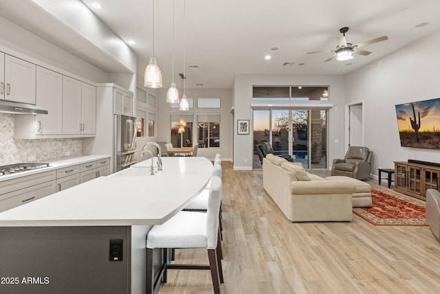 kitchen with a kitchen breakfast bar, appliances with stainless steel finishes, tasteful backsplash, a kitchen island with sink, and pendant lighting