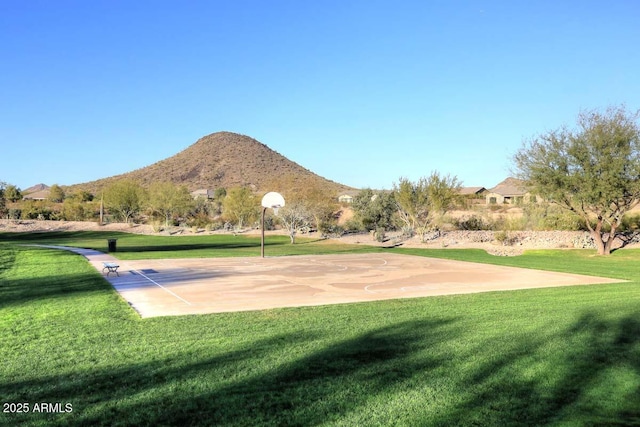 surrounding community featuring basketball hoop, a mountain view, and a yard