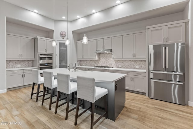 kitchen with tasteful backsplash, pendant lighting, a kitchen bar, a kitchen island with sink, and appliances with stainless steel finishes