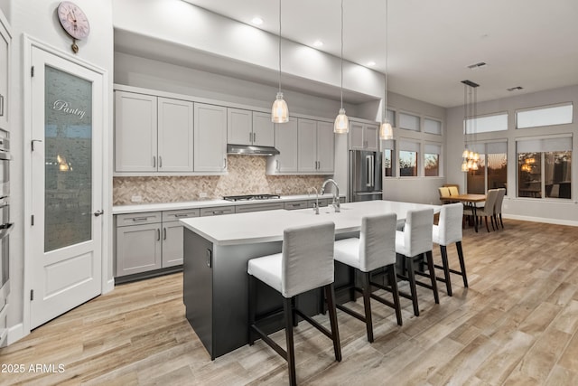 kitchen with a center island with sink, decorative light fixtures, gray cabinets, and appliances with stainless steel finishes