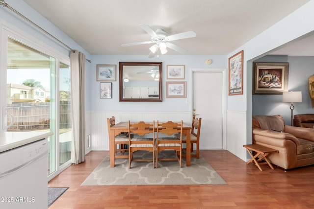 dining area with a wainscoted wall, ceiling fan, and light wood-style flooring