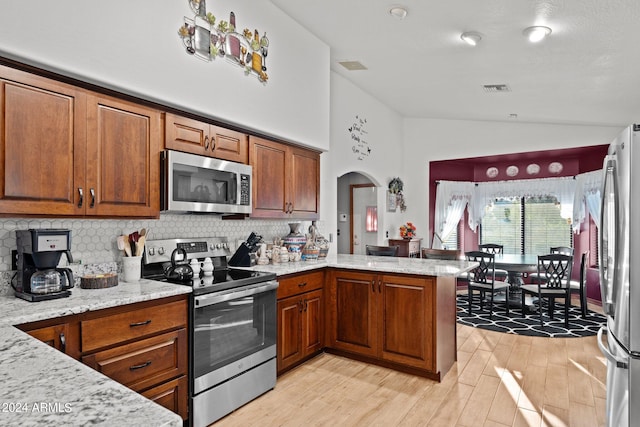 kitchen featuring light stone counters, lofted ceiling, kitchen peninsula, light hardwood / wood-style flooring, and appliances with stainless steel finishes